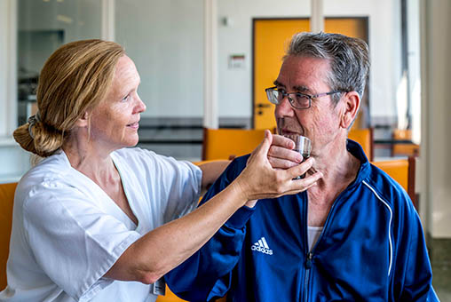 Eine Pflegemitarbeiterin hilft einem älteren Mann behutsam beim Trinken - Albertinen Haus - Medizinisch-Geriatrische Klinik 