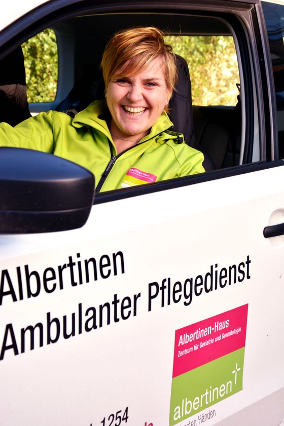 Eine Mitarbeiterin des Albertinen Ambulater Pflegedienst blick lächelnd aus einem Dienstfahrzeug