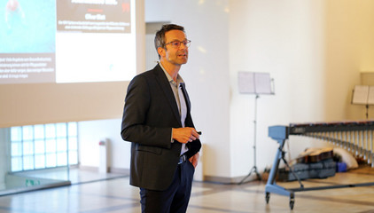 Prof. Dr. Michael Denkinger spricht zum Publikum vor einer Projektsleinwand beim Einführungssymposium „Die Zukunft ist alt!“ von Priv.-Doz. Dr. Gödel, Chefarzt der Klinik für Geriatrie im Albertinen Zentrum für Altersmedizin im Albertinen Krankenhaus in Hamburg. Prof. Dr. Michael Denkinger spricht zum Publikum vor einer Projektsleinwand beim Einführungssymposium „Die Zukunft ist alt!“ von Priv.-Doz. Dr. Gödel, Chefarzt der Klinik für Geriatrie im Albertinen Zentrum für Altersmedizin im Albertinen Krankenhaus in Hamburg.