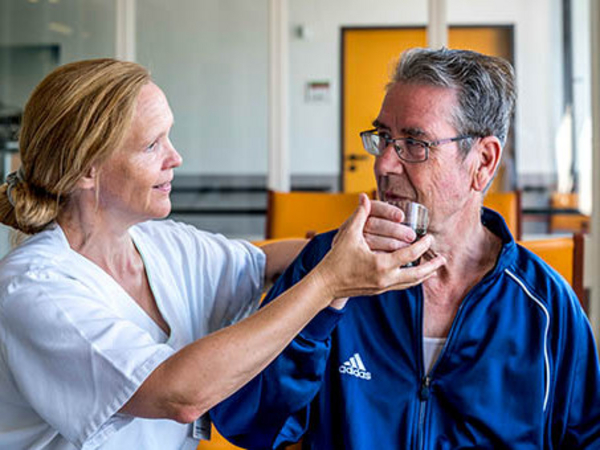Eine Pflegemitarbeiterin hilft einem älteren Mann behutsam beim Trinken - Albertinen Haus - Medizinisch-Geriatrische Klinik 