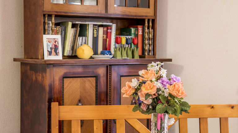 Blumenvase auf Tisch, dahinter Schrank mit Büchern - Max Herz Haus