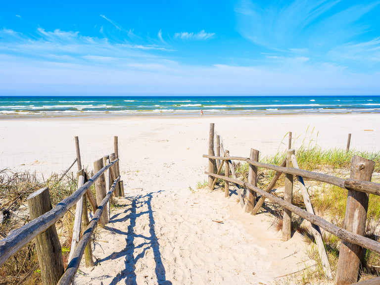 Blick durch den Aufgang zum Strand hin zum Meer, symbolisch für den Start in die Sommerferien