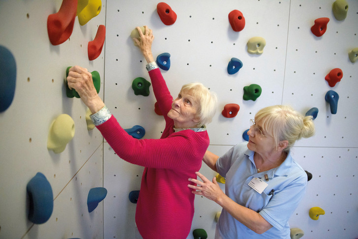 Patientin übt an Boulderwand unter fachlicher Anleitung