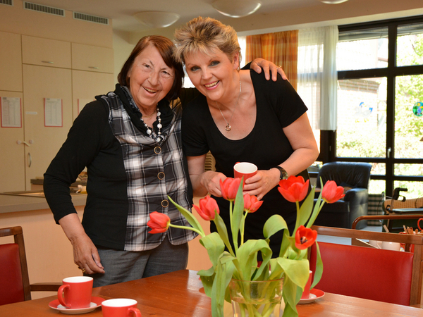 Mitarbeiterin und Bewohnerin stehen an einem Tisch mit Blumen - Albertinen Haus in Hamburg