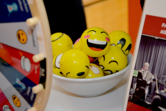 Mehrere gelbe Anti-Stress-Bälle mit Smiley-Bemalung in einer Schale am Stand des Albertinen Hauses beim Eimsbütteler Seniorentag neben Flyern und einem Quizrad