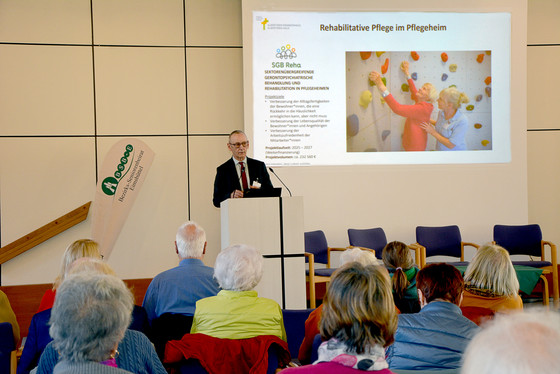 Geschäftsführer Ralf Zastrau stellt am Rednerpult neben einer Leinwand das Albertinen Haus vor dem Publikum in den Stuhlreihen vor