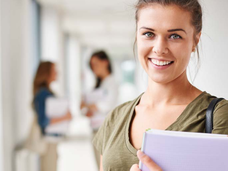 Eine Teilnehmerin blickt auf einem Gang mit weiteren Menschen mit einem Laptop in der Hand lächelnd in die Kamera als Titelmotiv zum Kursprogramm 2027 mit Seminaren, Fort- und Weiterbildungen für das Gesundheitswesen der Albertinen Akademie in Hamburg-Schnelsen.